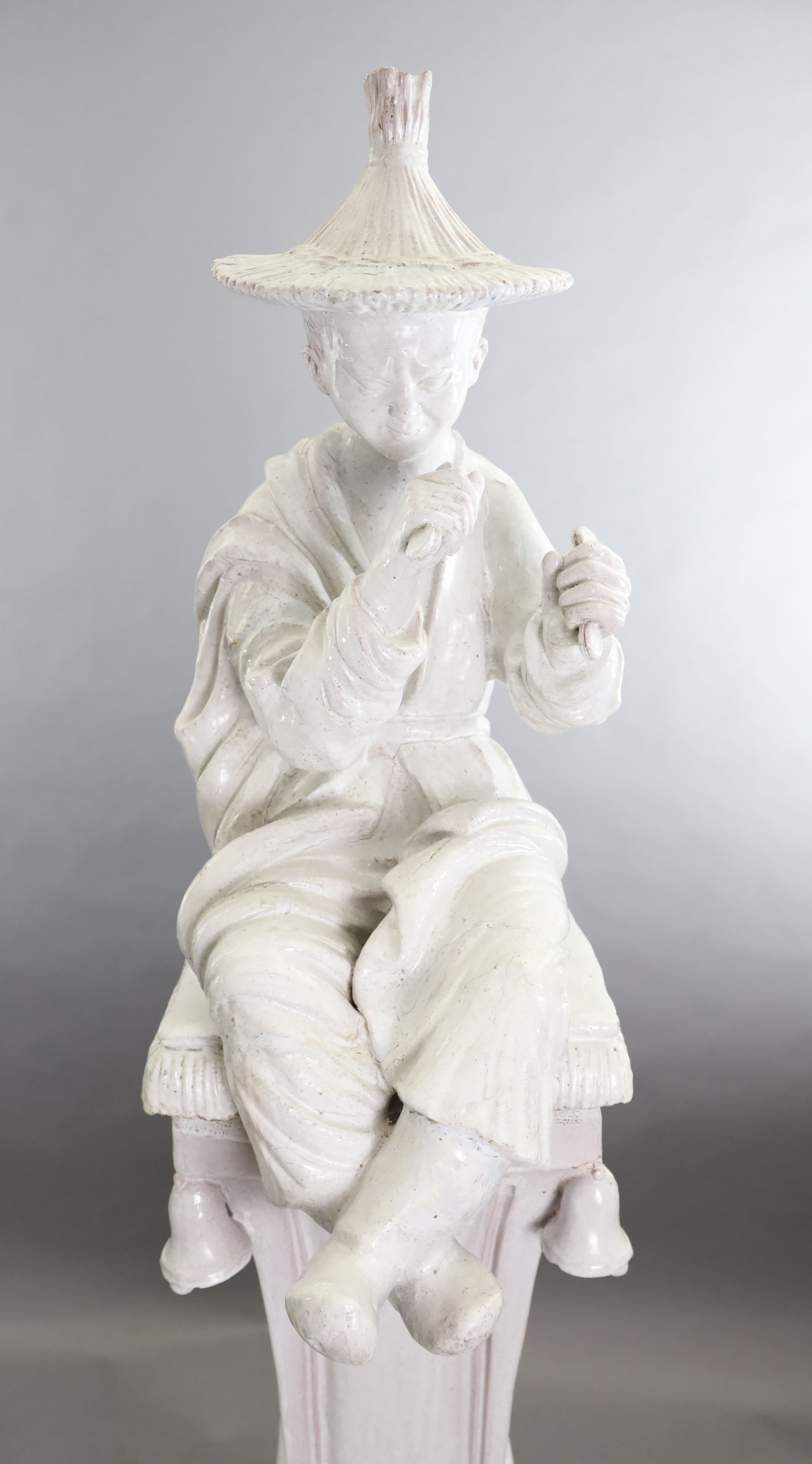 A pair of Continental tin glazed pottery figures of a Chinese man and woman, seated upon a bell-fringed pedestals, D.1ft 8in. H.6ft 1in